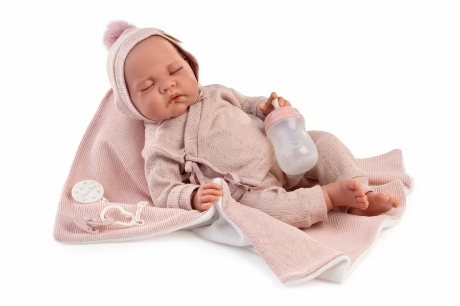 Muñeca Recién Nacida Luna de Antonio Juan dormida sobre toquilla rosa con biberón, gorro con pompón y chupete