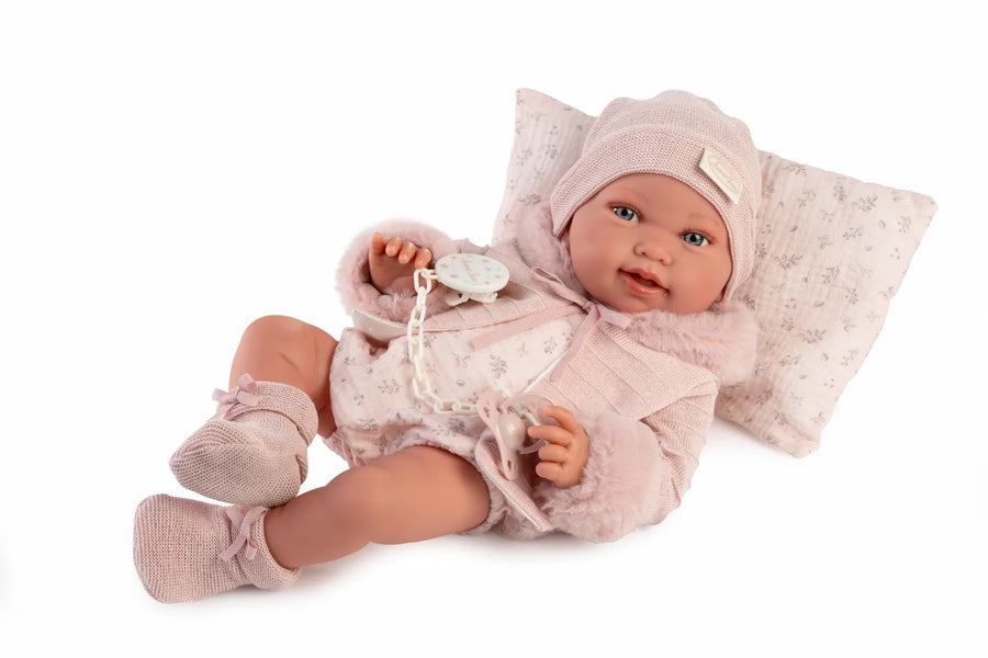 Muñeca Recién Nacida Pipa invierno de Antonio Juan tumbada sobre cojín con gorro, chaqueta rosa y chupete