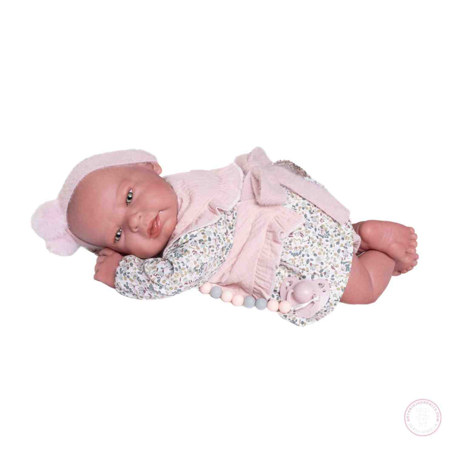Muñeca Sweet Reborn Lea de Antonio Juan tumbada de lado con vestido de flores, gorro rosa y chupete