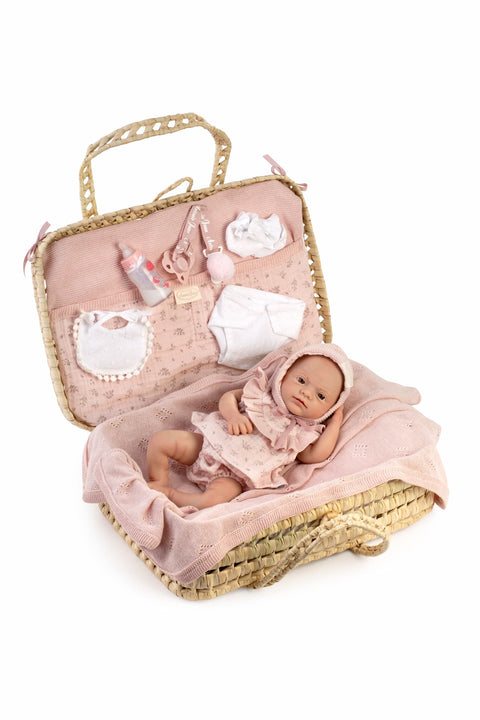 Muñeca reborn de silicona Violeta con ojos marrones y toquilla rosa palo, dentro de su maletín artesanal de palma abierto en cunita