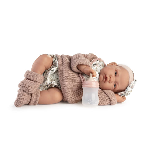 Muñeca Recién Nacida Lúa de Antonio Juan tumbada de lado con jersey rosa de punto, peúcos y biberón
