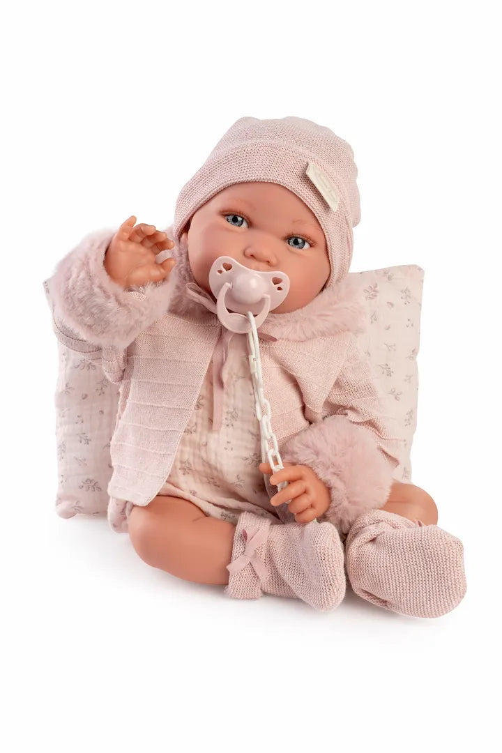 Muñeca Recién Nacida Pipa invierno de Antonio Juan sentada con chupete, gorro rosa y cojín estampado