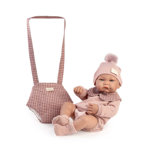 Muñeca Recién Nacida Nica de Antonio Juan con gorro de pompón rosa junto a su portabebé de cuadros