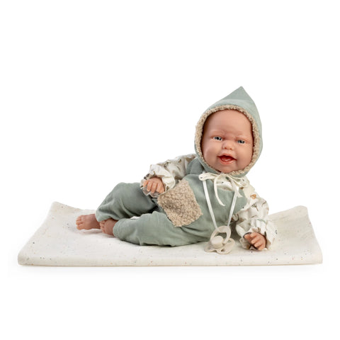 Muñeca Clara de Muñecas Antonio Juan con peto verde, capucha de borreguito y chupete, tumbada sobre su mantita