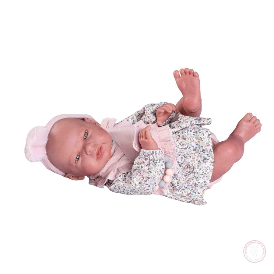 Muñeca Sweet Reborn Lea de Antonio Juan tumbada con vestido floral, babero rosa y diadema con pompón