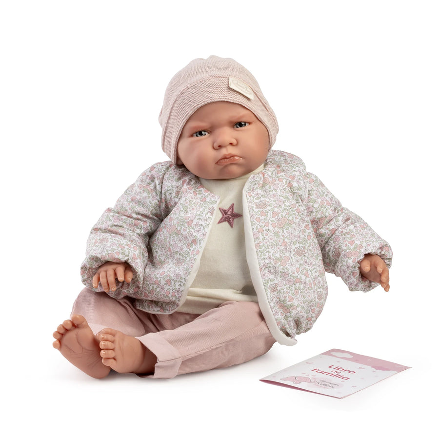 Muñeca Mi Primer Reborn Berta de Antonio Juan sentada con bomber de flores, gorro rosa y libro de familia